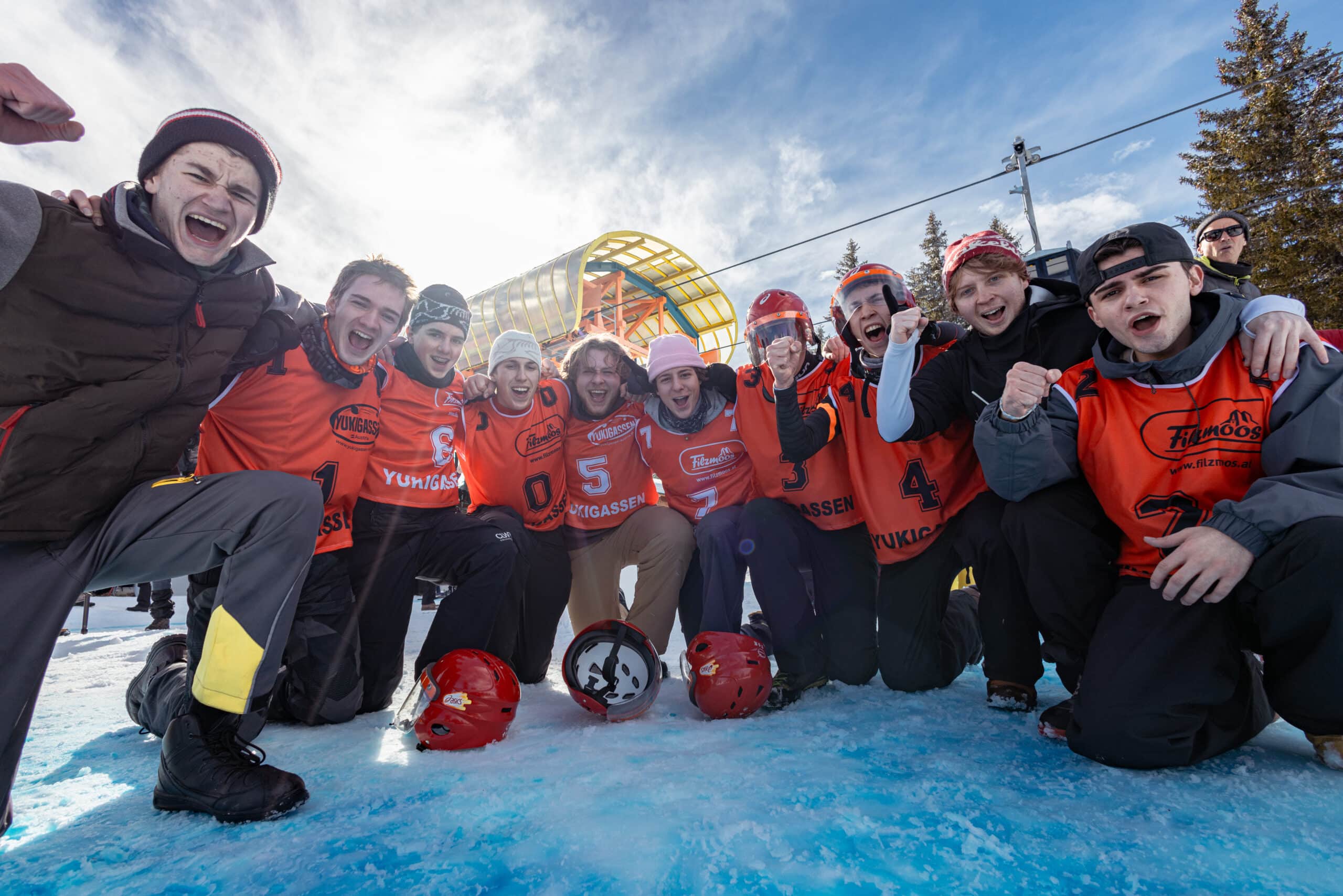 25_filzmoos_winter_event_yukigassen_3 Jubelnde Gruppe von Jugendlichen in Sportkleidung feiert gemeinsam im Schnee nach einem Winter-Event.