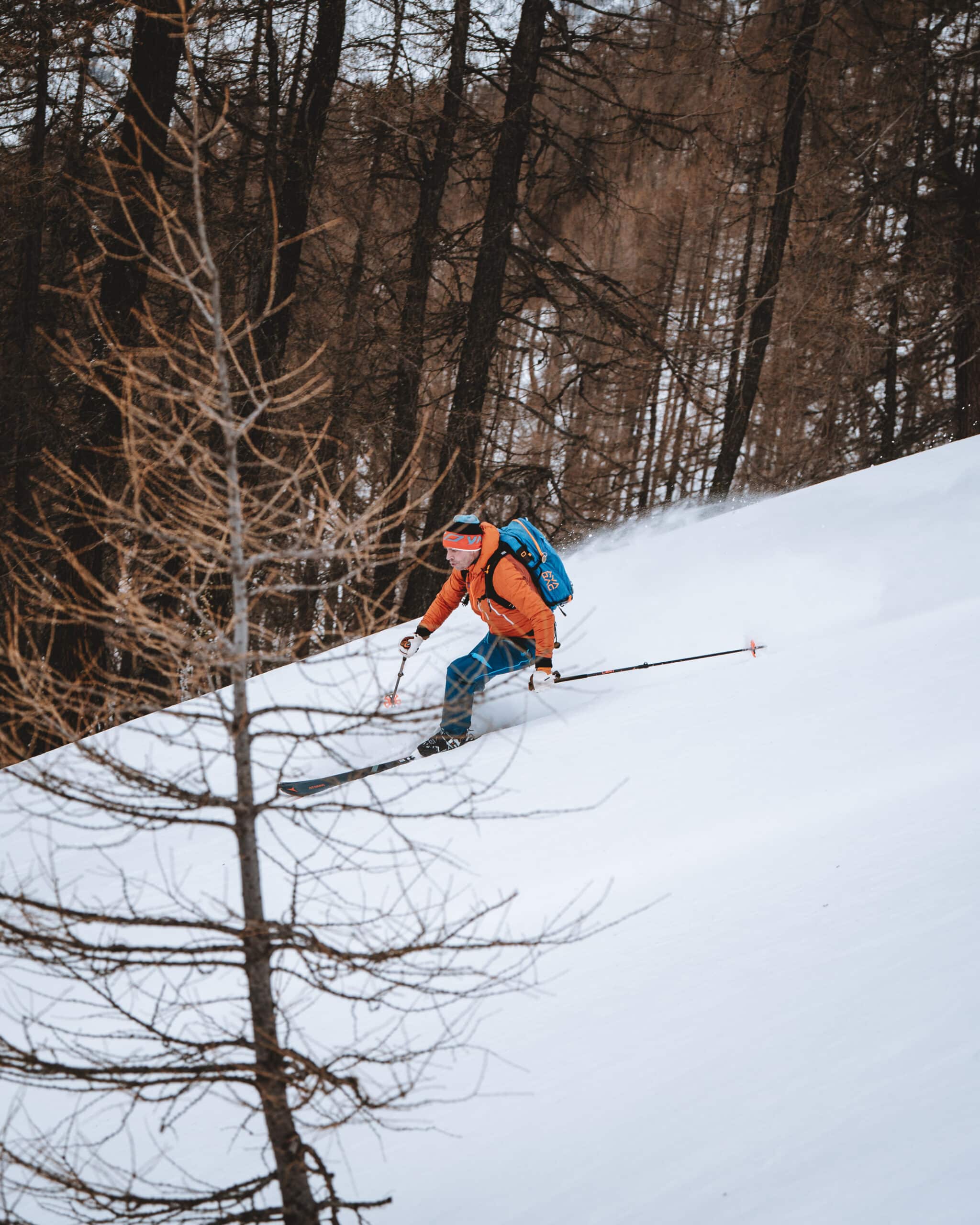 Bergzeit Frischluftkick Skifahrer fährt durch tiefen Schnee an einem bewaldeten Hang mit kahlen Winterbäumen.