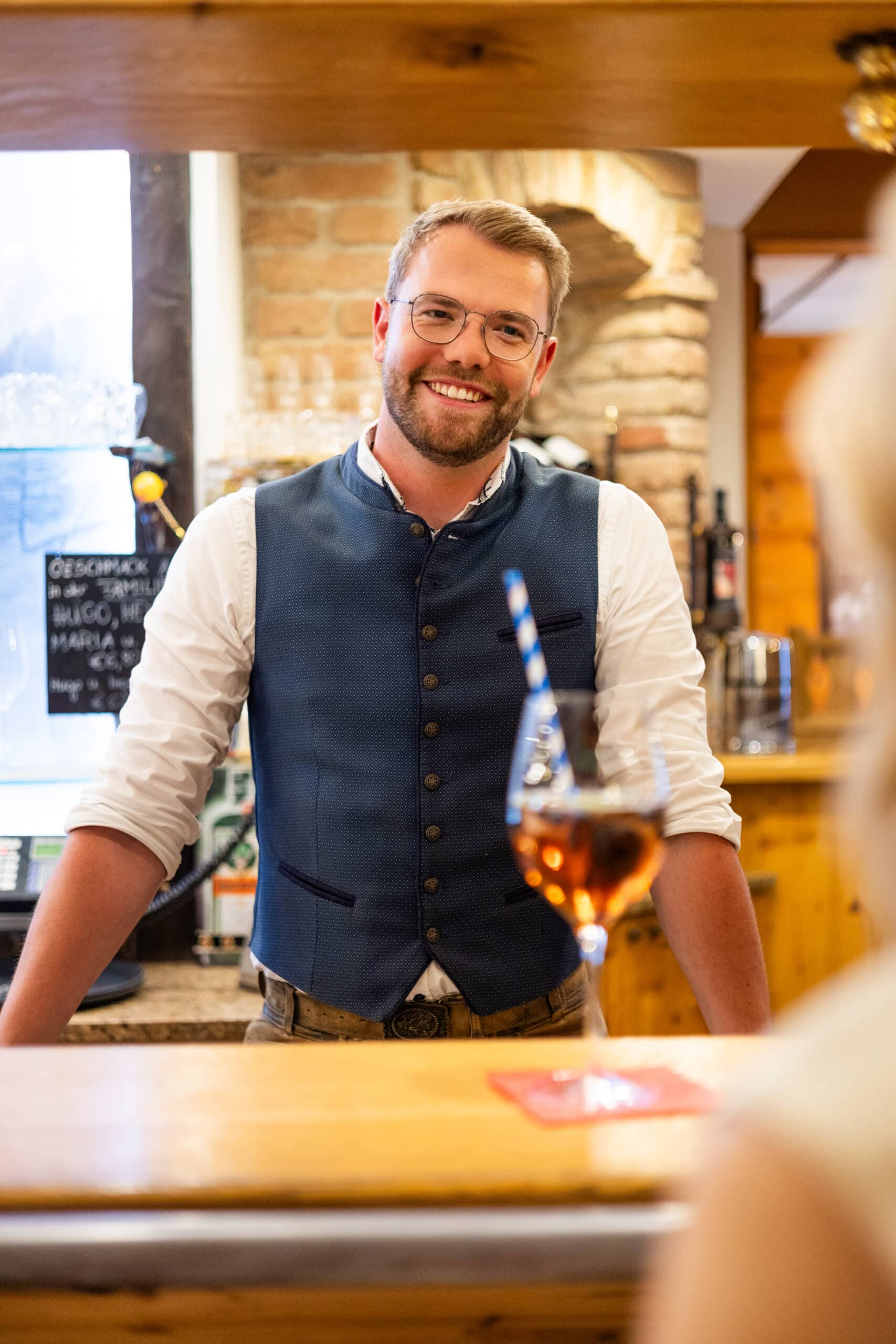 Bar_Bischofsmütze Final-5 Barmitarbeiter steht hinter einer Schank und lächelt