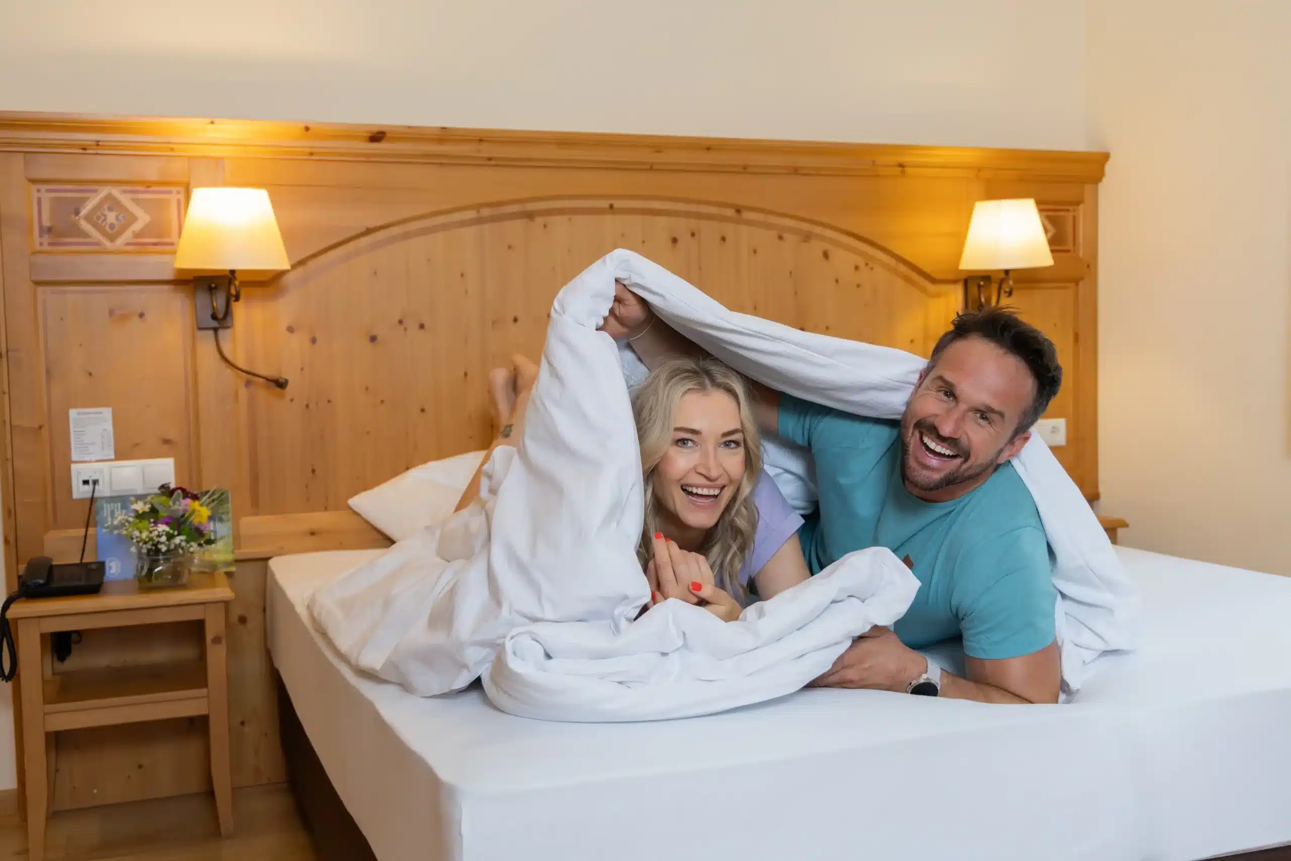 Zufriedene Urlaubsgäste sitzen Junior Deluxe Suite in Filzmoos Glückliche Urlaubsgäste liegen am Bett der Junior Deluxe Suite im Hotel Bischofsmütze, Filzmoos